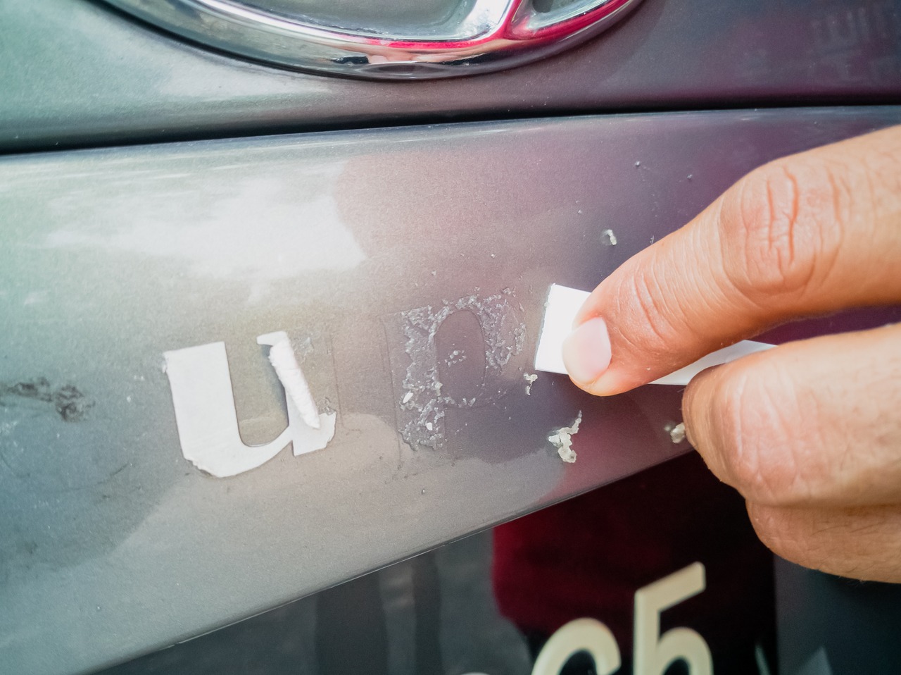 Someone removes an adhesive sticker from the back of a car